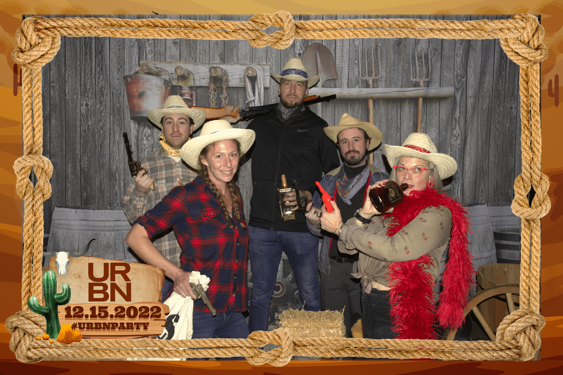 Old Time Photo Experience 11 Five people dressed in cowboy costumes pose with toy guns and props in a Western-themed photo booth, surrounded by a rope border with text reading URBN 12.15.2022 #URBNPARTY in the corner.
